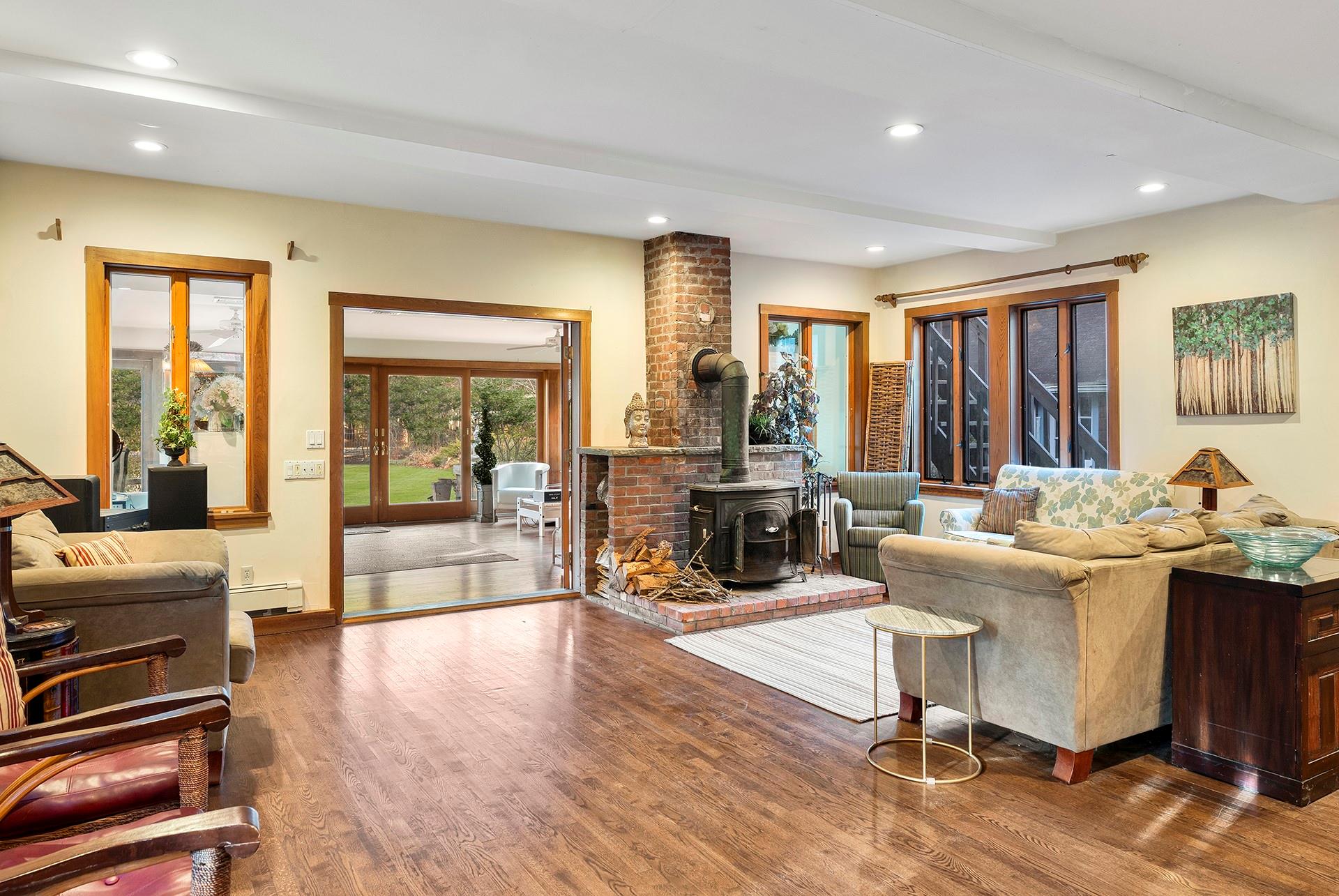 61 Lower 7 Ponds Road Water Mill, NY 11976 - Photo 16 of 43 Living room featuring a wood stove, wood finished floors, recessed lighting, a baseboard radiator, and beam ceiling