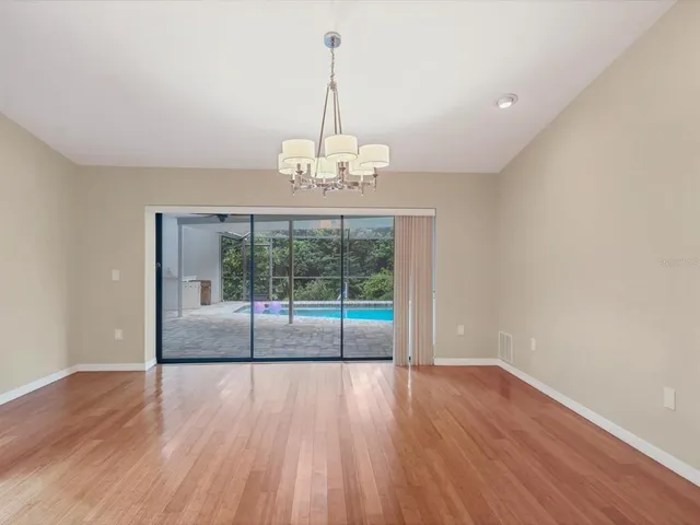 a view of an empty room with wooden floor and a kitchen