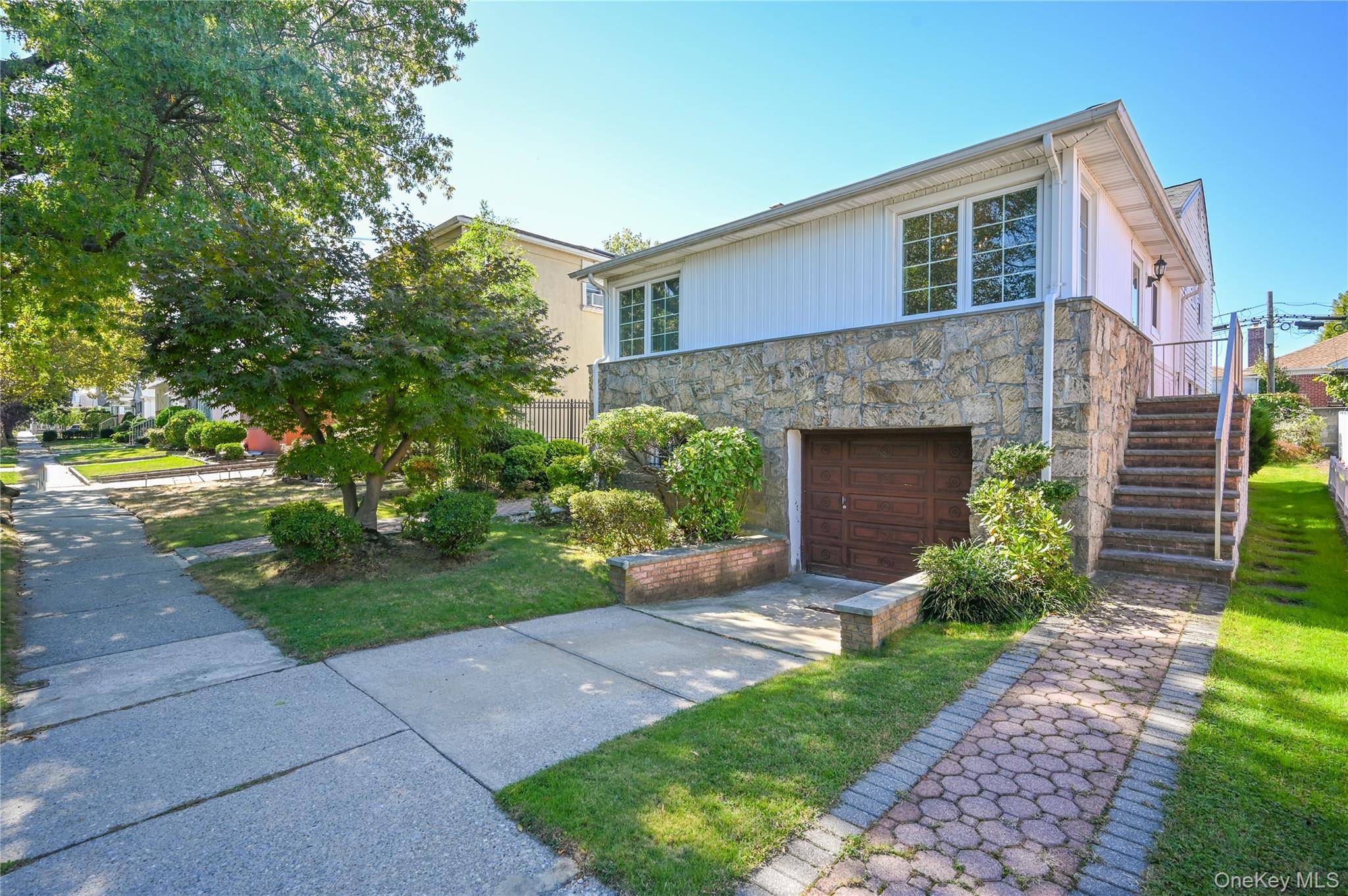 28-30 210th Street Queens, NY 11360 - Photo 1 of 19 View of front of home with stairs, stone siding, driveway, an attached garage, and a front lawn