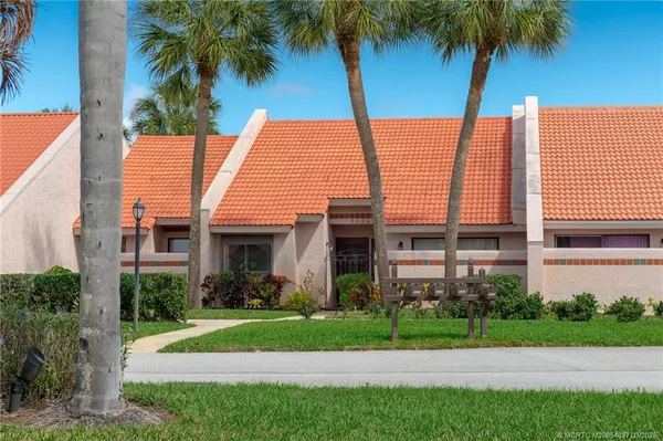 a view of a house in front of a yard with plants and palm trees