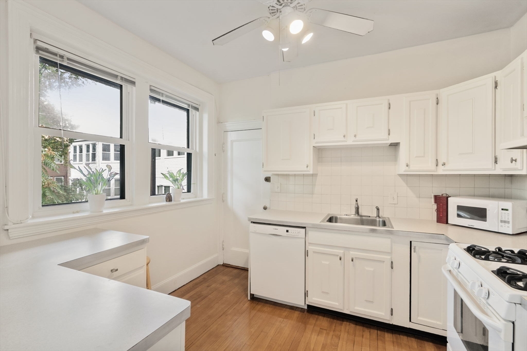 114 St Paul Street, Unit 5 Brookline, MA 02446 - Photo 9 of 22 a kitchen with a sink dishwasher stove and white cabinets with wooden floor