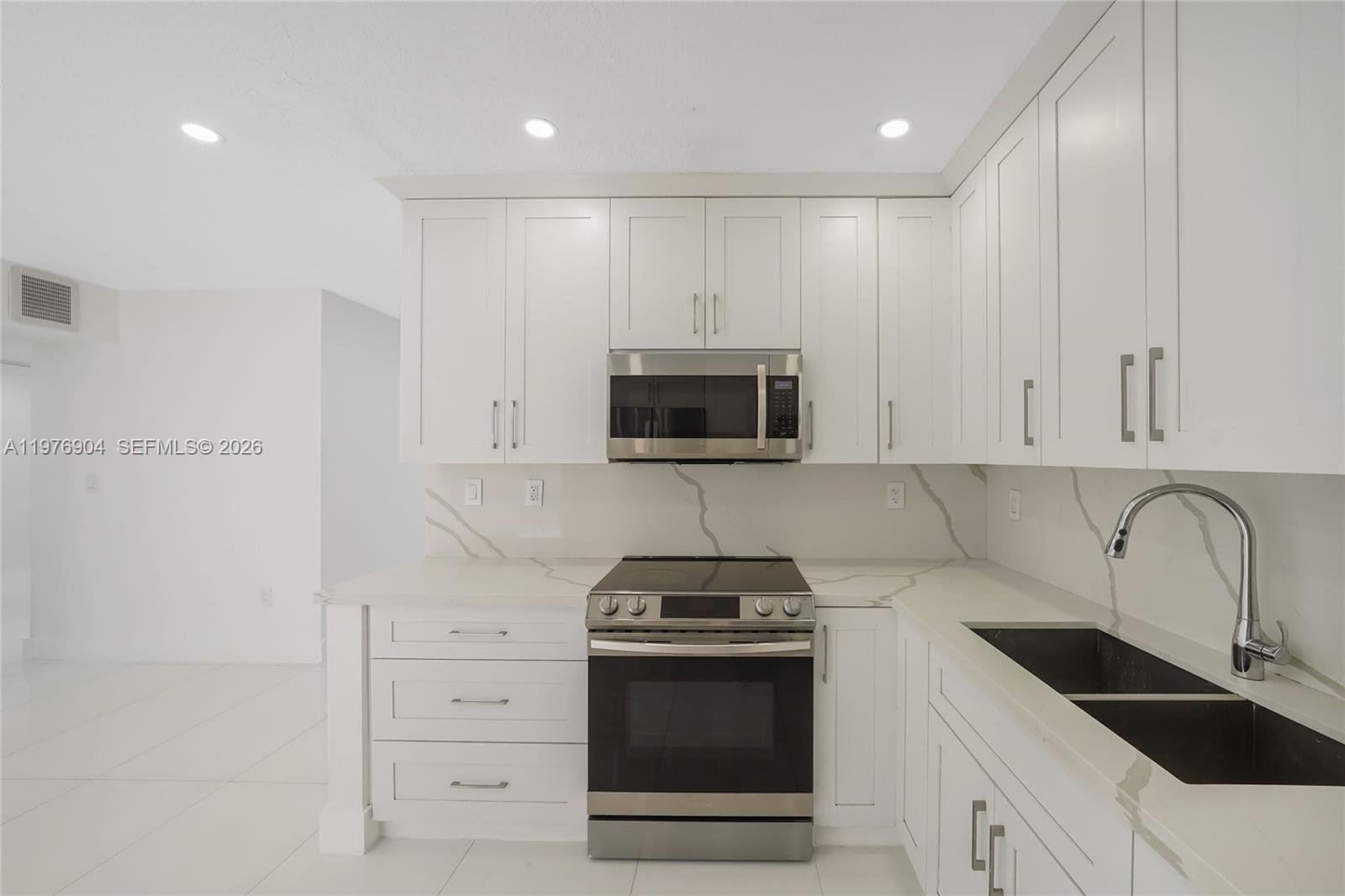 5635 West 13th Court Hialeah, FL 33012 - Photo 9 of 47 a kitchen with granite countertop white cabinets and stainless steel appliances