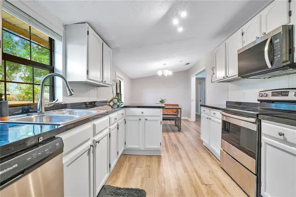 a kitchen with a sink dishwasher stove and white cabinets with wooden floor