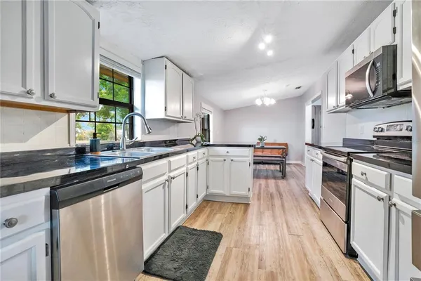 a kitchen with stainless steel appliances granite countertop wooden cabinets a sink dishwasher a stove and a refrigerator with wooden floor