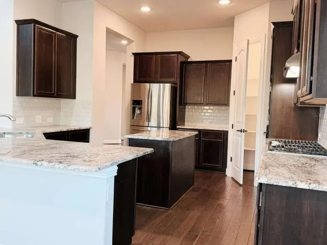 a kitchen with stainless steel appliances kitchen island granite countertop a refrigerator a stove and a sink with wooden floor