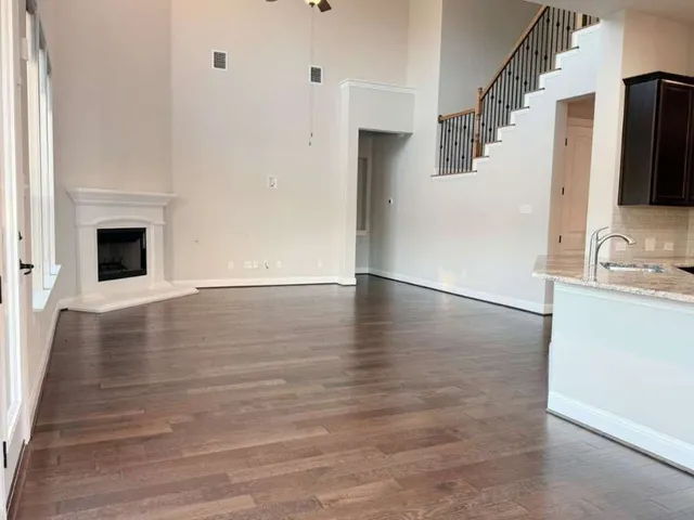 a view of an empty room with wooden floor and a kitchen