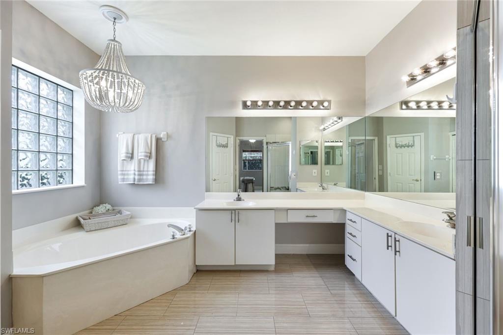 697 Crossfield Circle Naples, FL 34104 - Photo 13 of 18 Full bath featuring a garden tub, double vanity, a stall shower, and a chandelier