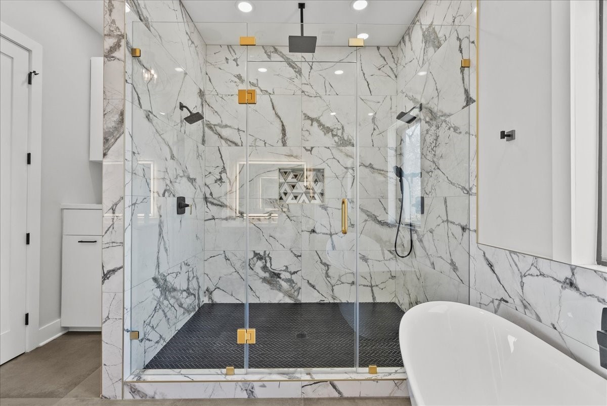 516 Reinerman Street Houston, TX 77007 - Photo 28 of 42 This bathroom features a luxurious walk-in shower with elegant marble tiles, gold accents, and a glass door. A modern freestanding bathtub complements the sophisticated design.