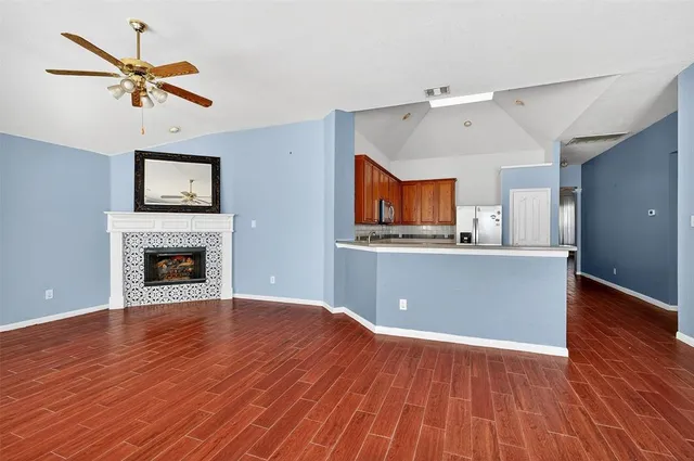 a view of a livingroom with a fireplace a ceiling fan and wooden floor