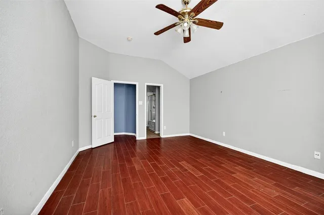 a view of an empty room with wooden floor and a ceiling fan