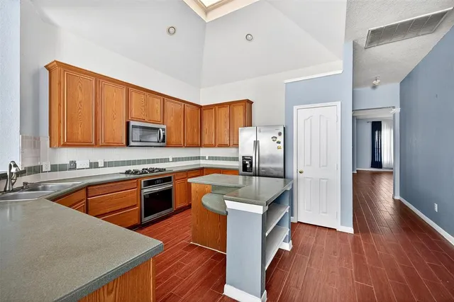 a kitchen with stainless steel appliances granite countertop a refrigerator a sink dishwasher a stove and white countertops with wooden floor