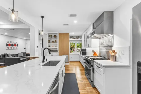 a kitchen with stainless steel appliances a sink dishwasher a stove a dining table and chairs with wooden floor