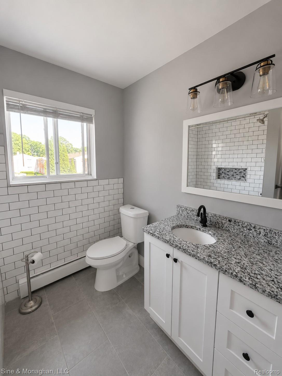 433 Miller Avenue, Unit 203 Rochester, MI 48307 - Photo 9 of 12 Bathroom featuring subway tile wainscoting, a white vanity with a speckled countertop, matte black hardware, and a modern three-light fixture