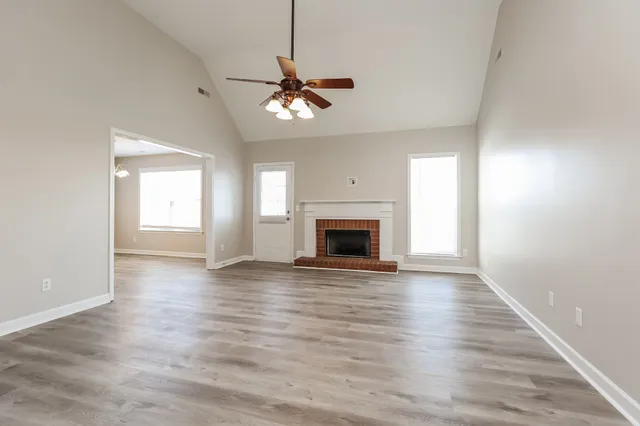 an empty room with wooden floor fireplace and windows