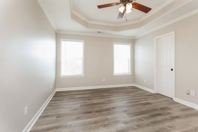 an empty room with wooden floor chandelier fan and windows