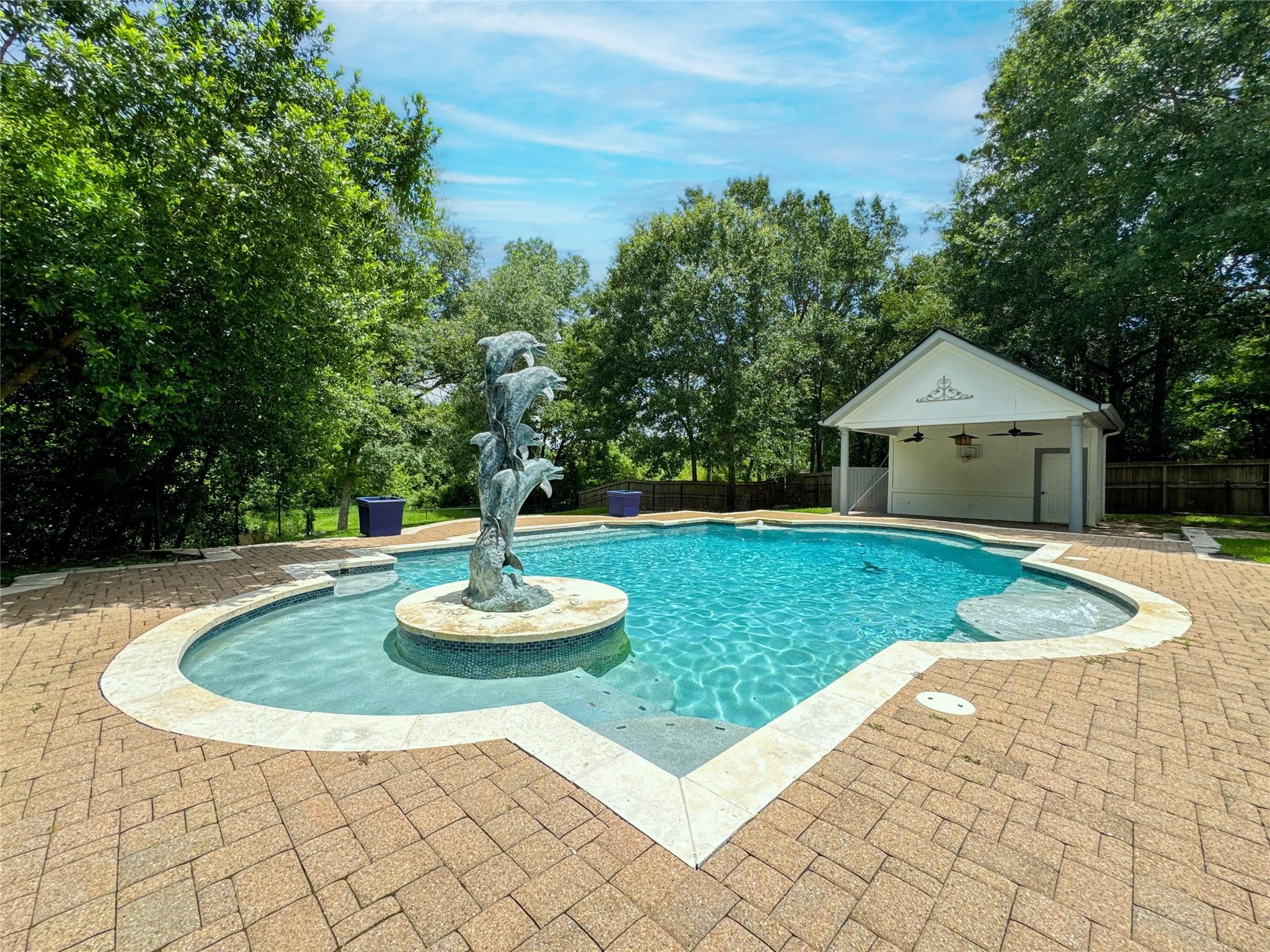1810 Woerner Road Houston, TX 77090 - Photo 36 of 39 This photo showcases a spacious backyard with a uniquely shaped pool featuring a central dolphin sculpture. The area is surrounded by greenery, providing a serene and private atmosphere. There's also a covered pavilion with ceiling fans, perfect for outdoor gatherings.