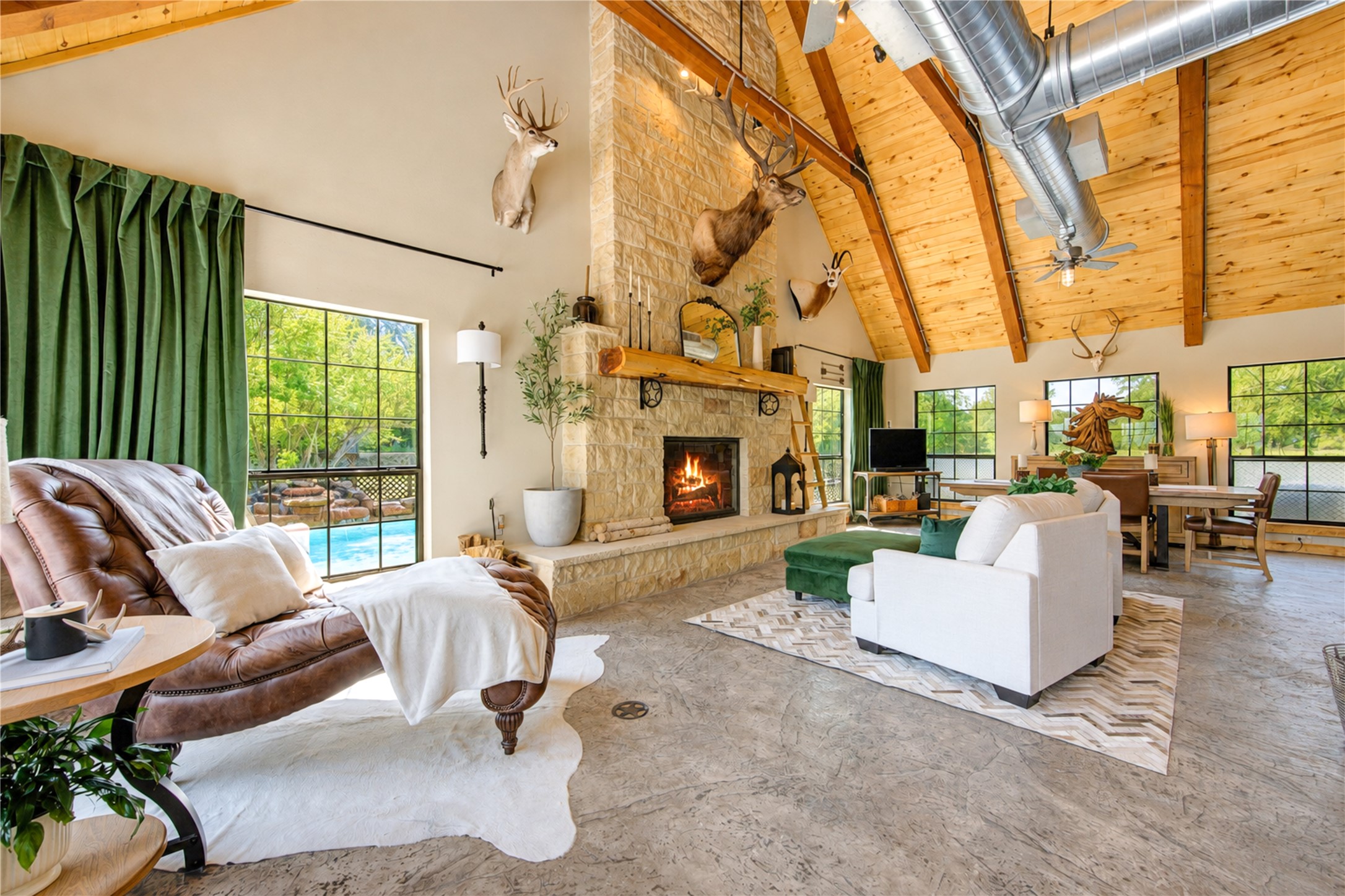 This Great Room features a massive limestone fireplace with live-edge wood mantel. Overhead, a vaulted wood-clad ceiling with exposed wood beams to add warmth and architectural character.
