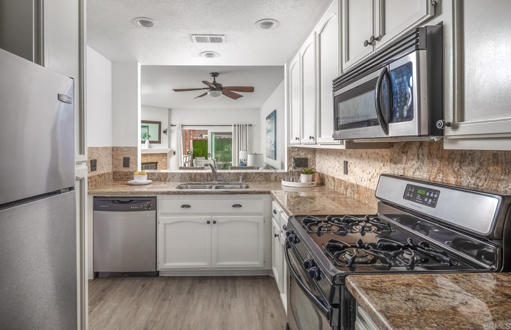 7777 Caminito Monarca, Unit 105 Carlsbad, CA 92009 - Photo 7 of 25 a kitchen with stainless steel appliances granite countertop a stove a sink dishwasher a refrigerator and white cabinets with wooden floor