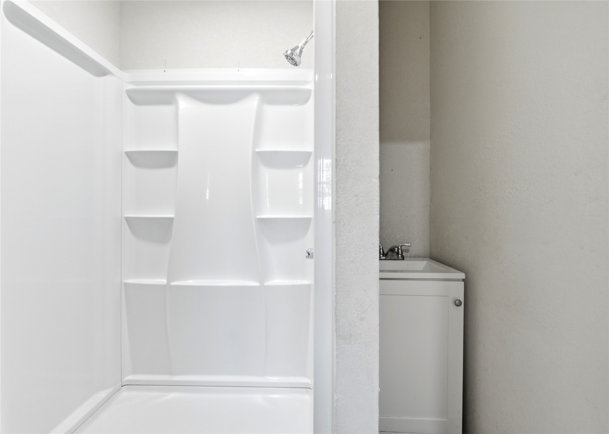 9403 Spaulding Street Houston, TX 77016 - Photo 43 of 50 This photo shows a simple bathroom with a white shower stall featuring built-in shelves and a small adjacent vanity with a sink.