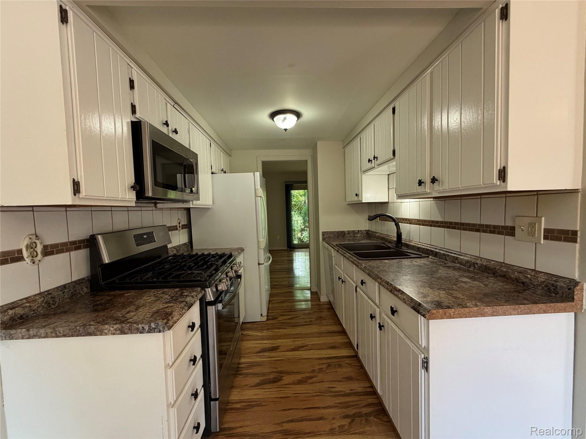 629 Oakbrook West, Unit 18 Rochester, MI 48307 - Photo 11 of 22 Galley kitchen featuring white cabinetry, stone-look countertops, stainless steel appliances, and wood-finish flooring