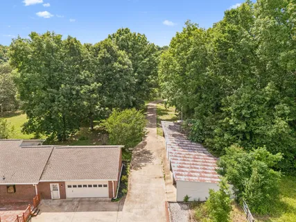 an aerial view of a residential houses with outdoor space and trees all around
