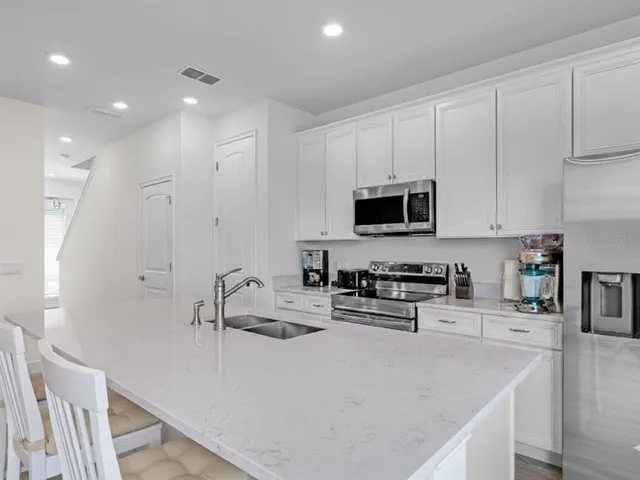 a kitchen with stainless steel appliances granite countertop a sink a stove top oven a refrigerator and white cabinets