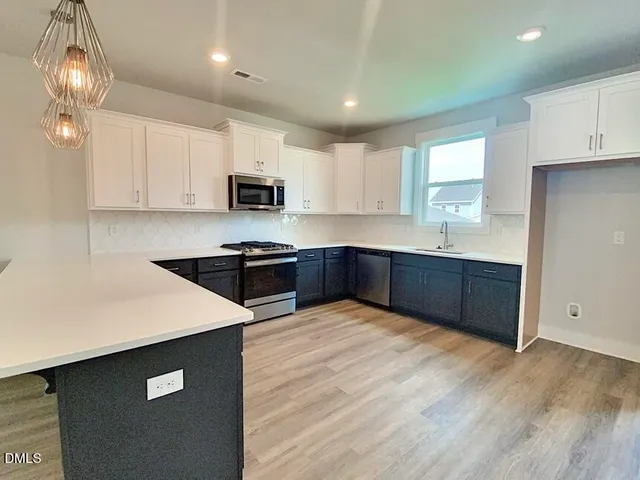 a kitchen with stainless steel appliances granite countertop a sink dishwasher a stove and a refrigerator with wooden floor