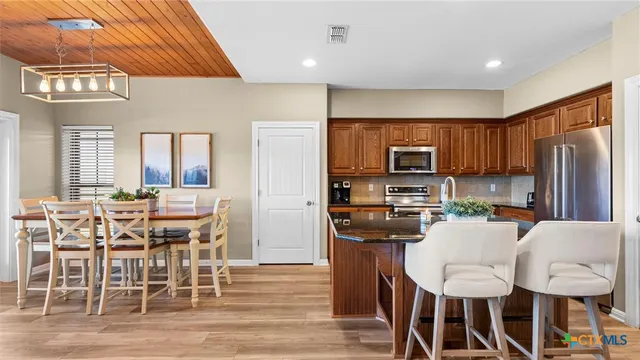 a kitchen with stainless steel appliances a dining table chairs refrigerator and sink