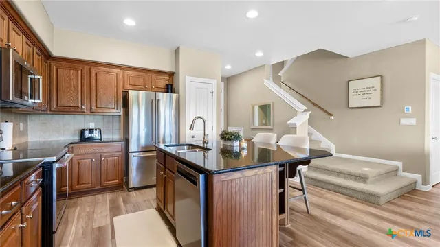 a kitchen with stainless steel appliances granite countertop a refrigerator a stove and a sink with wooden floor