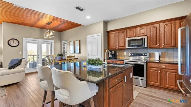 a kitchen with stainless steel appliances granite countertop a stove top oven a sink dishwasher a dining table and chairs with wooden floor