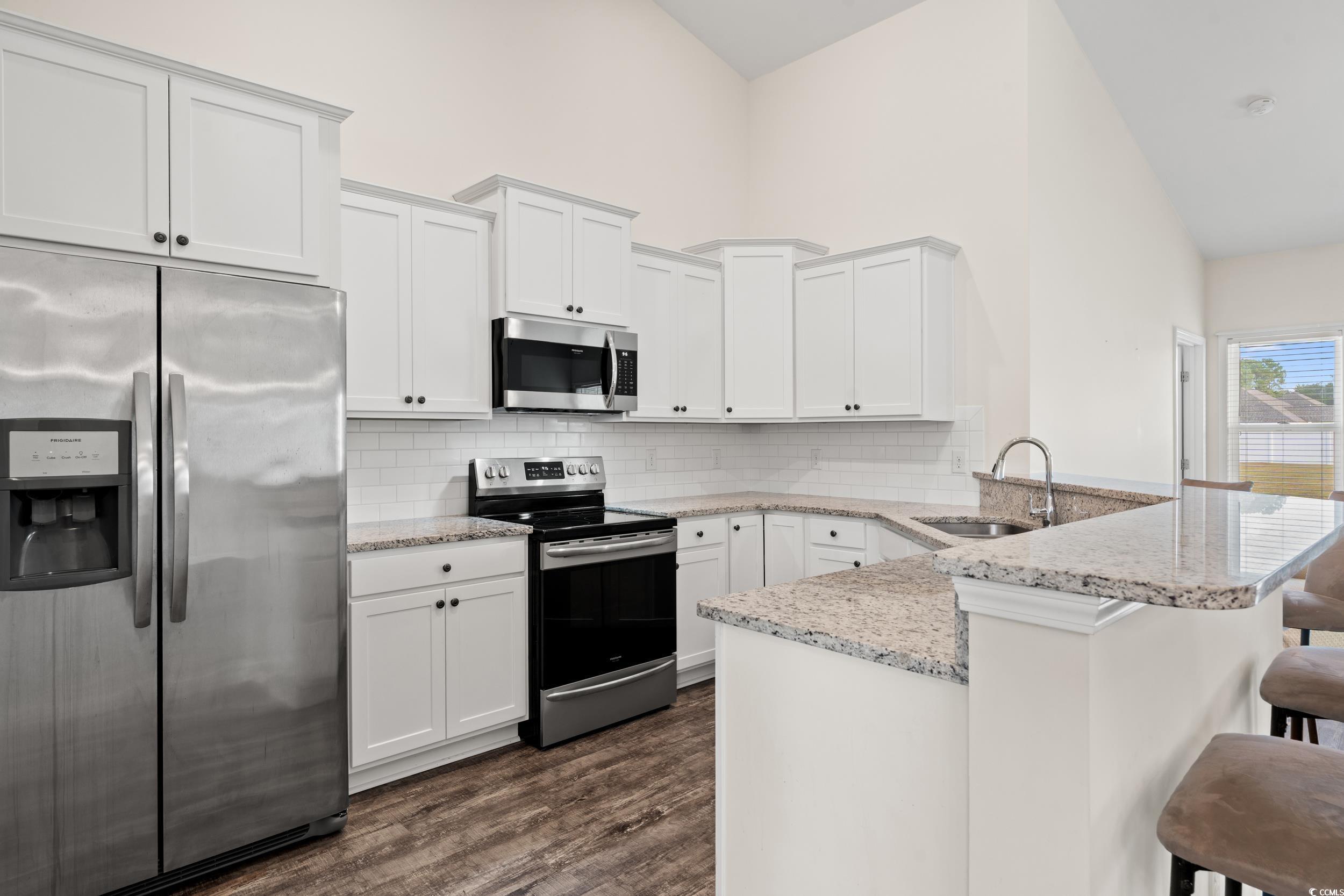 327 Fox Bay Road Loris, SC 29569 - Photo 7 of 23 Kitchen featuring a peninsula, stainless steel appliances, decorative backsplash, light stone counters, and high vaulted ceiling.