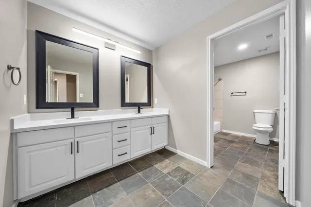 a spacious bathroom with a double vanity sink a mirror and a toilet