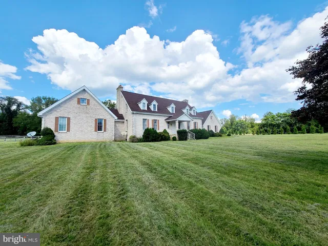 a view of a white house in front of a big yard with plants and large trees