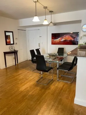 a living room with stainless steel appliances kitchen island granite countertop a couch a dining table and chairs with wooden floor