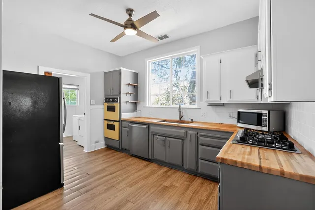 a kitchen with stainless steel appliances granite countertop a refrigerator a sink dishwasher a stove and white countertops with wooden floor