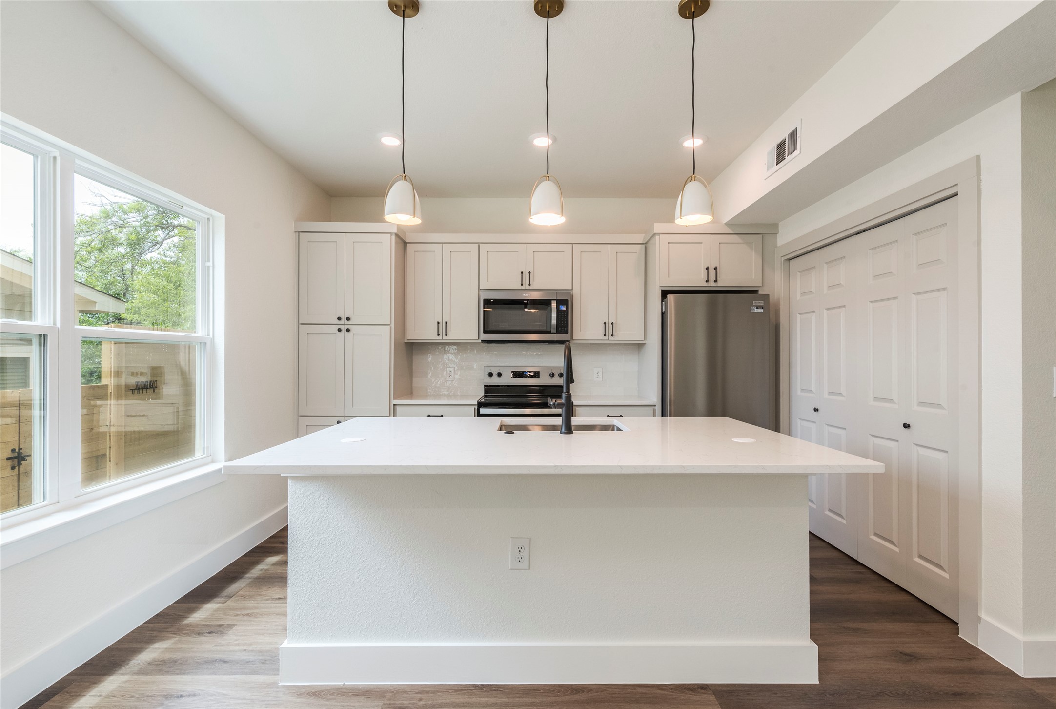 3702 Tower View Court, Unit A Austin, TX 78723 - Photo 1 of 1 Kitchen featuring appliances with stainless steel finishes, a sink, a center island with sink, light countertops, and dark wood-type flooring