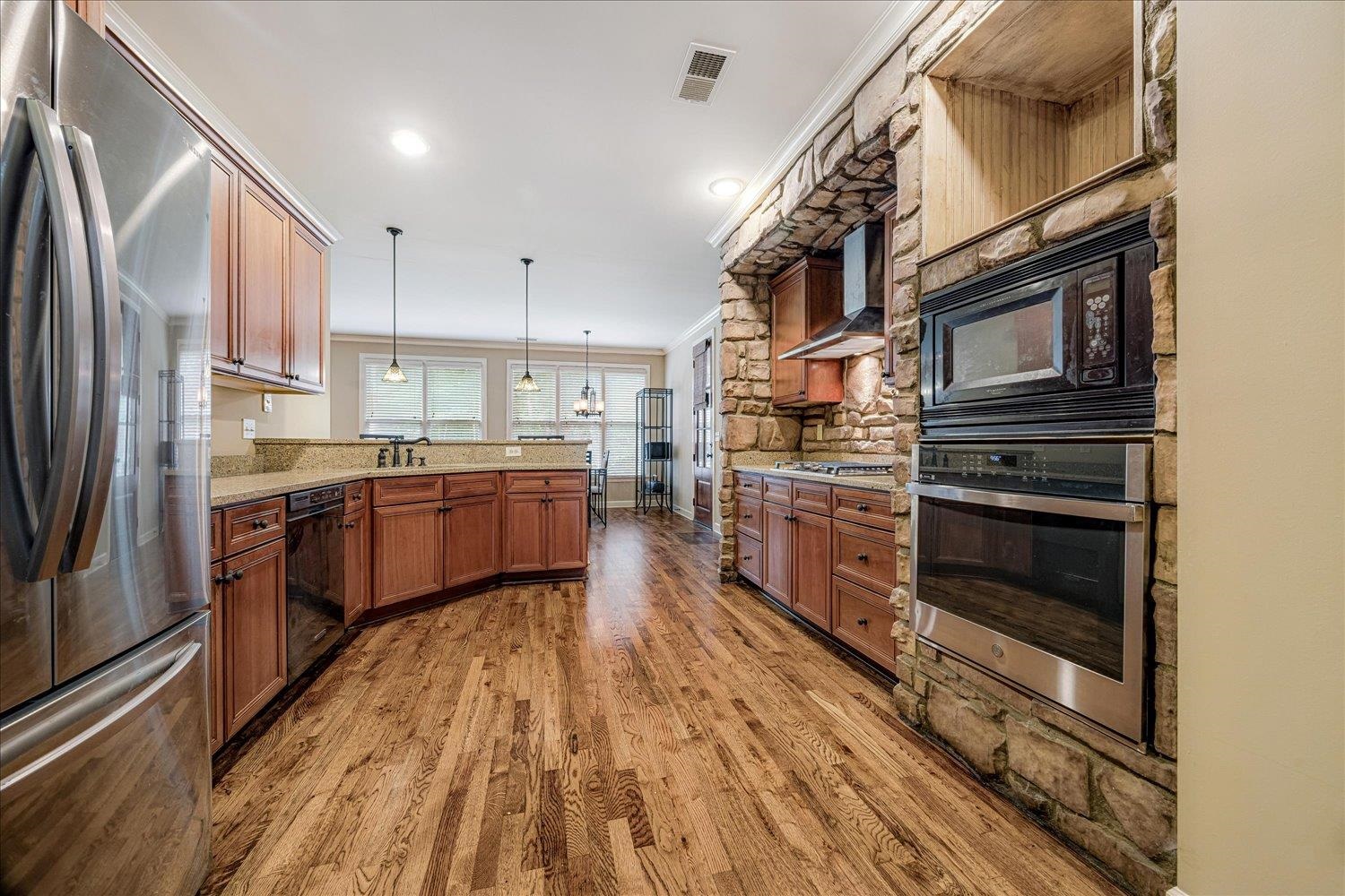 4597 Whisper Spring Drive Collierville, TN 38017 - Photo 15 of 40 Kitchen with ornamental molding, black appliances, brown cabinets, hanging light fixtures, and a peninsula