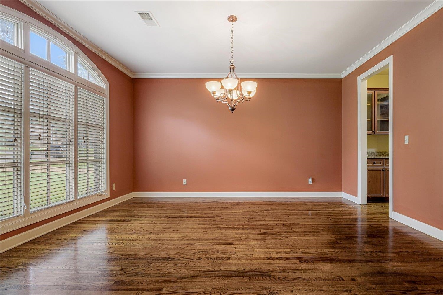 4597 Whisper Spring Drive Collierville, TN 38017 - Photo 9 of 40 Empty room with crown molding, dark wood-style flooring, and a chandelier