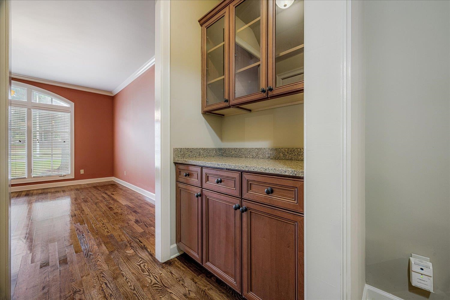 4597 Whisper Spring Drive Collierville, TN 38017 - Photo 10 of 40 Bar featuring brown cabinets, ornamental molding, light stone counters, glass insert cabinets, and dark wood-style flooring