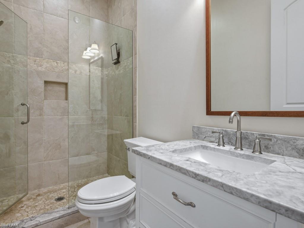 7051 Hunters Road Naples, FL 34109 - Photo 34 of 49 a bathroom with a granite countertop toilet a sink a mirror and shower