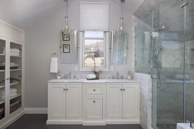 a bathroom with a granite countertop sink two mirror and shower