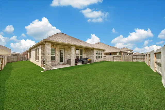 a view of a white house in front of a big yard with plants and large trees