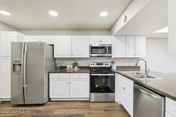 a kitchen with stainless steel appliances granite countertop a refrigerator stove a sink and white cabinets
