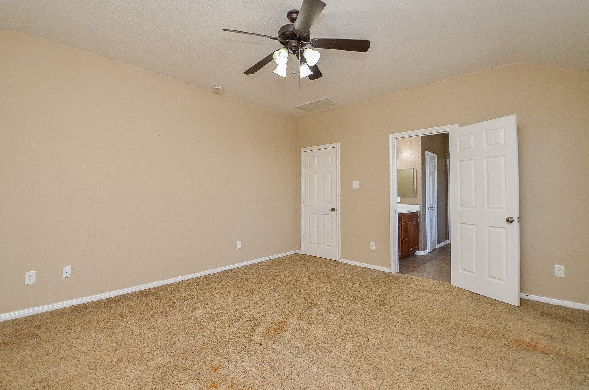 5411 Rio Drive Baytown, TX 77521 - Photo 22 of 30 Primary bedroom featuring neutral tones and a functional layout, ready for personalization. The room offers plush carpeting, soft beige walls, and a ceiling fan with integrated lighting for year-round comfort. Multiple doors provide convenient access to a closet and an en-suite bathroom, enhancing privacy and usability. Natural light and clean finishes create a bright, inviting atmosphere, making this a versatile retreat within the home.