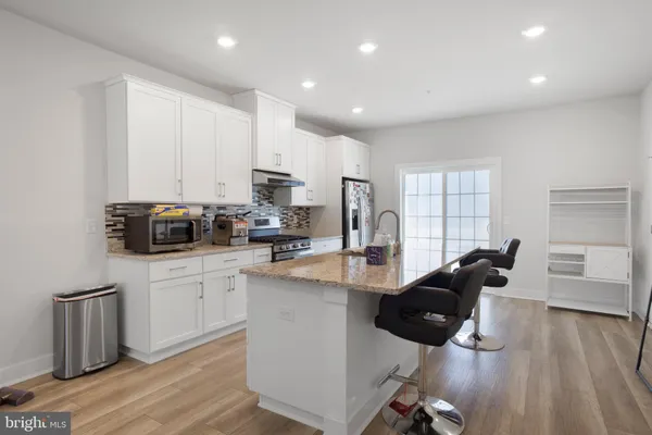 a kitchen with stainless steel appliances granite countertop a stove a sink a refrigerator and white cabinets with wooden floor