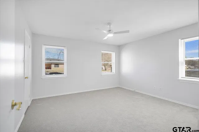 an empty room with a chandelier fan and windows
