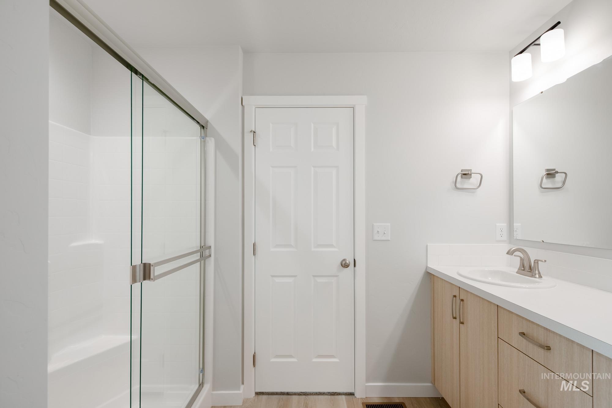 2391 West Fallon Loop Nampa, ID 83651 - Photo 18 of 20 Spacious bathroom featuring a glass-enclosed shower with integrated seating, a vanity with light wood-finish cabinetry, a white countertop, and a large mirror with contemporary lighting
