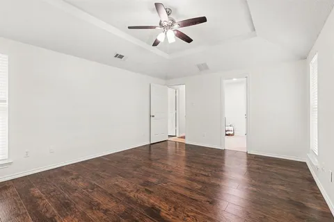 an empty room with wooden floor ceiling fan and window