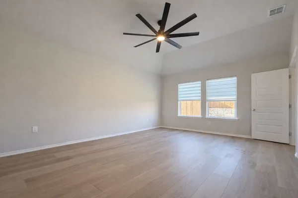an empty room with wooden floor ceiling fan and windows
