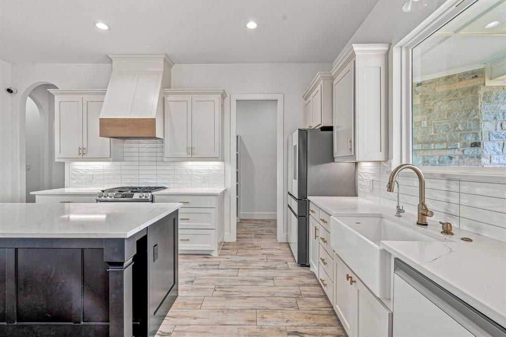 8140 Lavender Road Springtown, TX 76082 - Photo 11 of 40 Kitchen featuring a large island with a light-toned countertop, white cabinetry with gold-toned hardware, a farmhouse-style sink with a brass-finish faucet, and wood-finish flooring